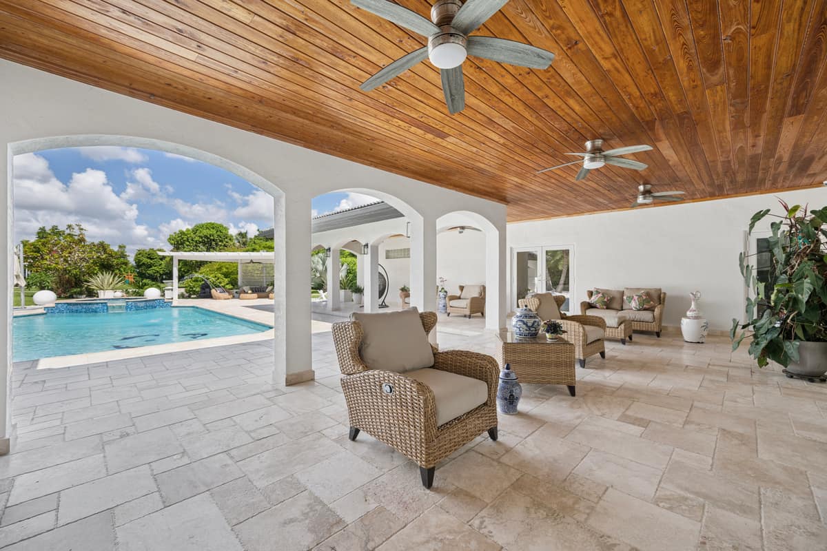 Covered travertine terrace with wicker seating overlooking a swimming pool