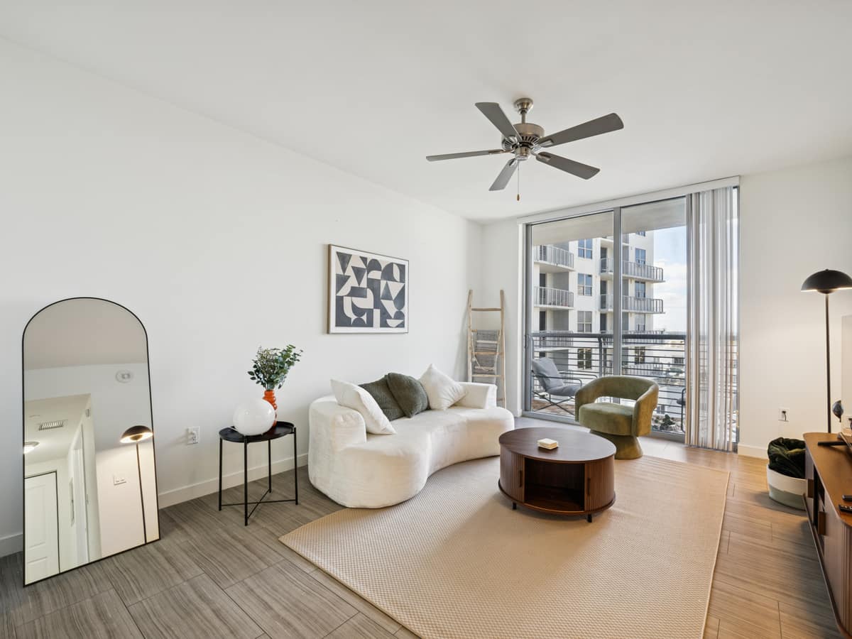 Sunlit condo living room with a curved sofa and floor-to-ceiling balcony doors